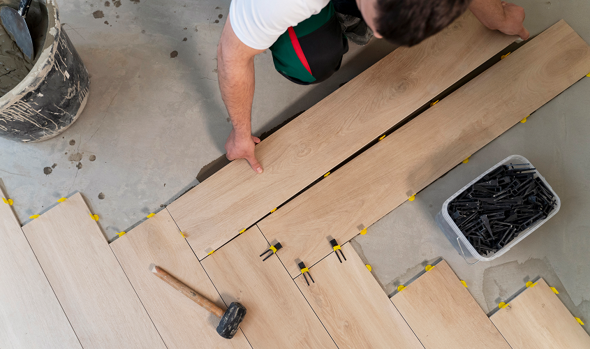 Installer positioning large-format wood-grain floor tiles using tile leveling clips and a rubber mallet.